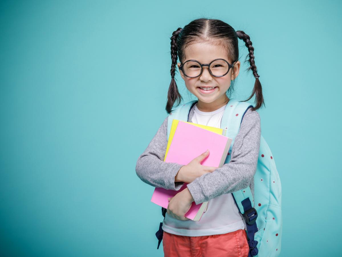 kindergarten girl carrying a backpack and books. 