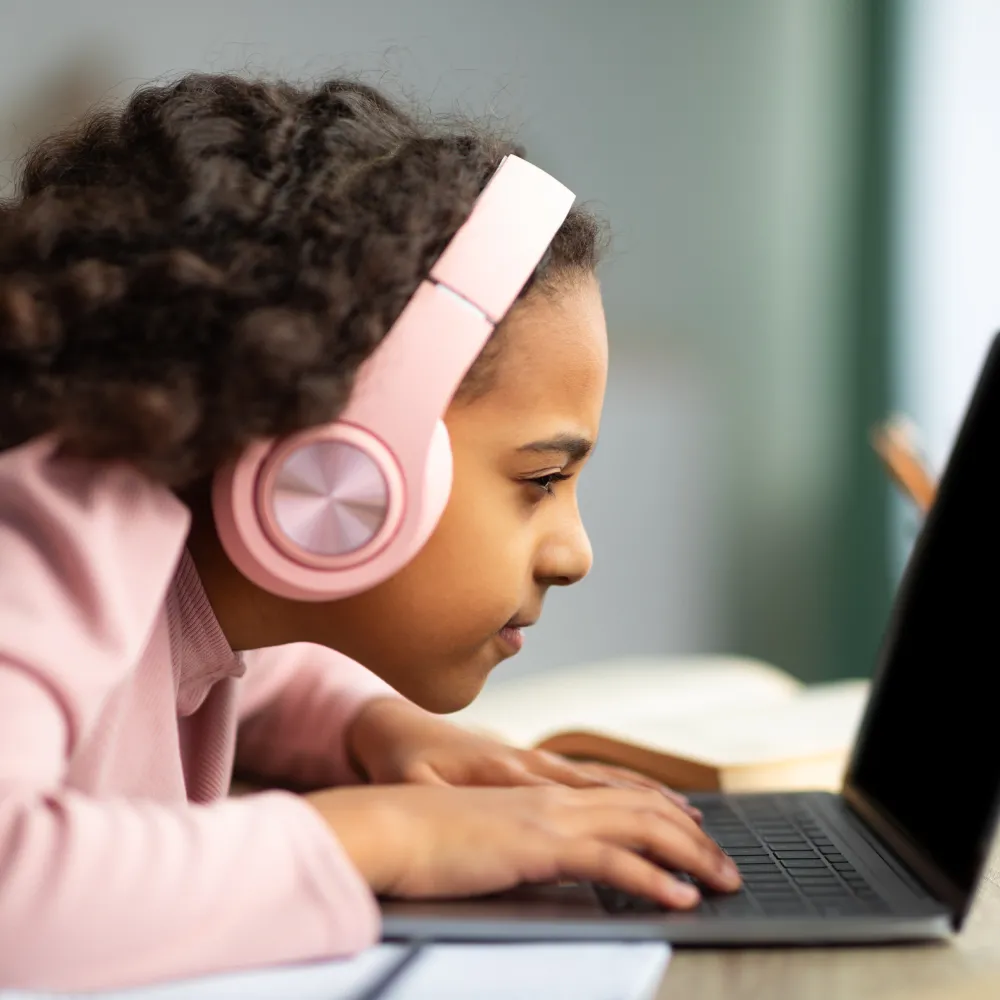 Young girl looking closely at her laptop with headphones on. 